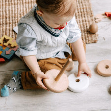Enfant assis au sol qui tient des jouets en bois 
